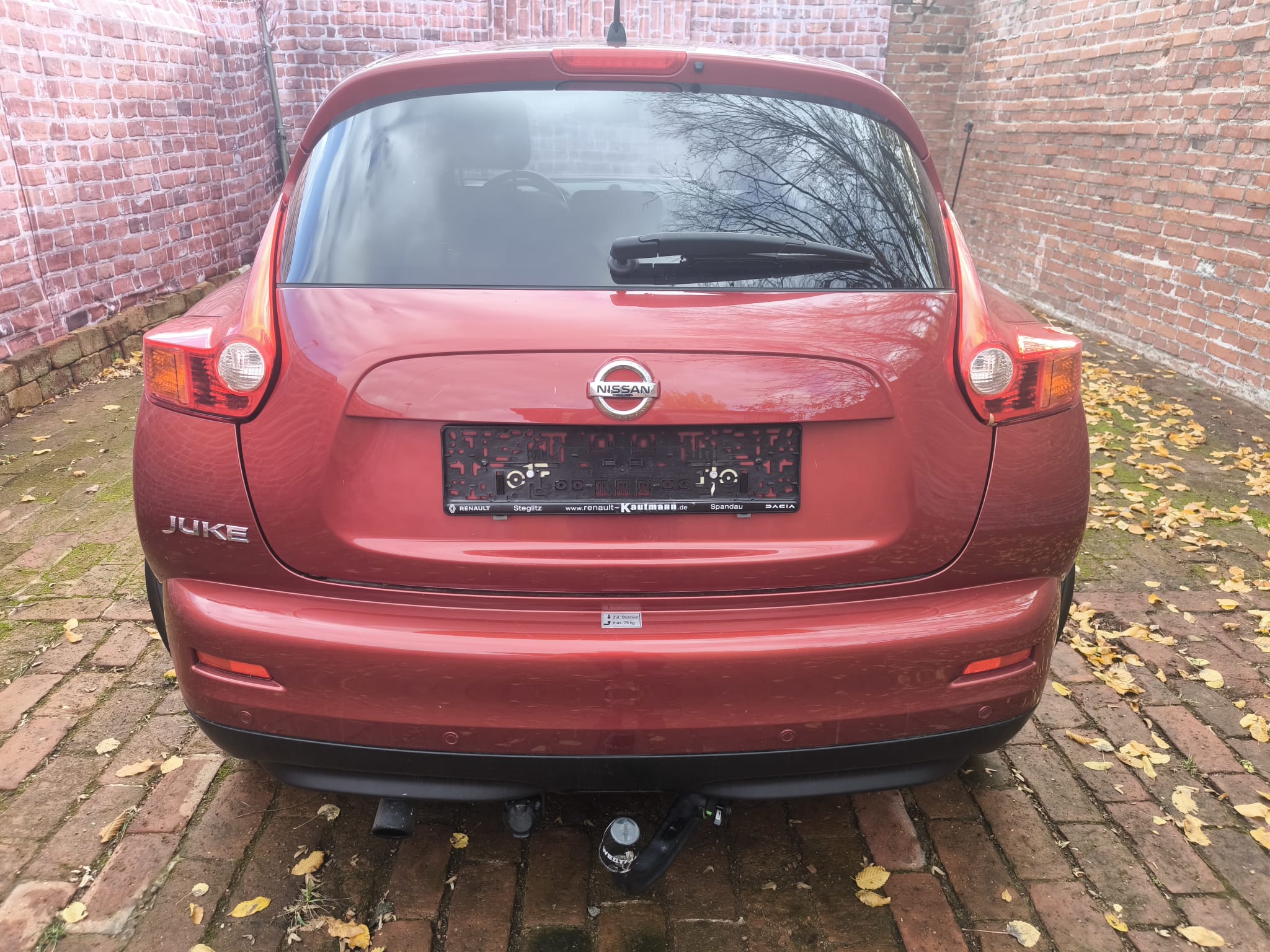 Nissan Juke als verkaufter Gebrauchtwagen in Hilden von hinten auf einem Hof mit Backsteinmauer