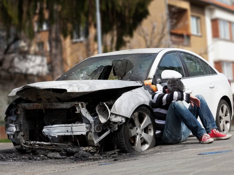 Mann sitzt am Auto mit Totalschaden