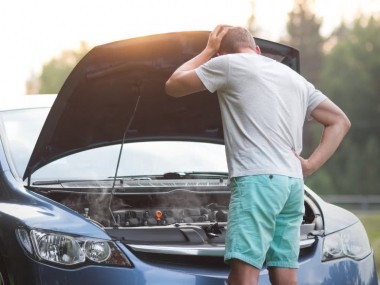 Mann steht vor dem Auto mit Motorschaden und versteht es nicht