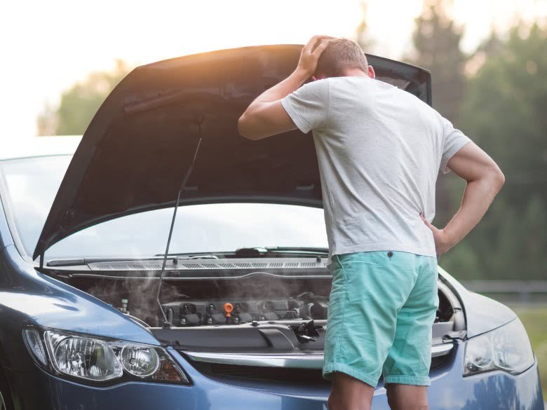 Mann steht vor dem Auto mit Motorschaden und versteht es nicht