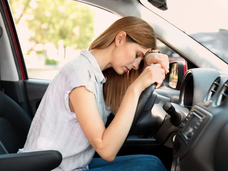 Frau verzweifelt am Lenkrad weil Motor läuft aber das Auto nicht losfährt