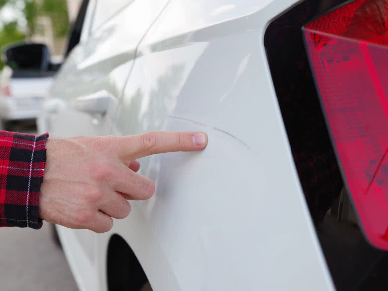 Finger zeigt auf einen Parkschaden-Kratzer am Auto